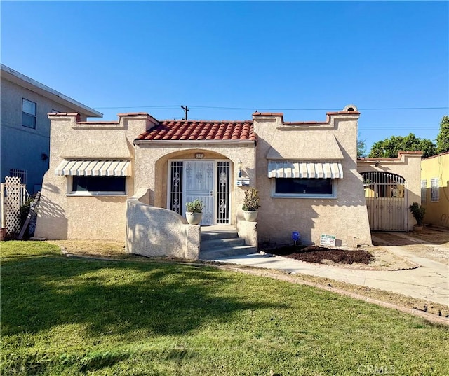 mediterranean / spanish-style house featuring a tiled roof, a gate, stucco siding, and a front yard