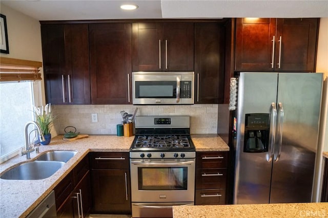 kitchen with light stone countertops, a sink, appliances with stainless steel finishes, and decorative backsplash