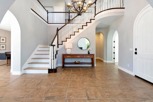 foyer entrance with arched walkways, a towering ceiling, baseboards, and stairway