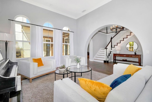 living area featuring crown molding, arched walkways, stairway, wood finished floors, and a notable chandelier