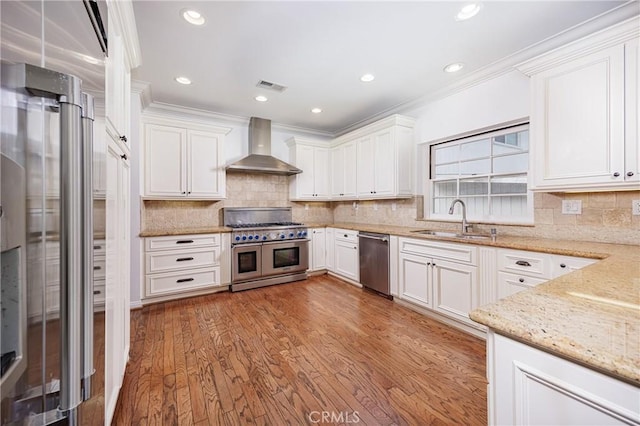 kitchen featuring visible vents, a sink, wall chimney range hood, stainless steel appliances, and light stone counters