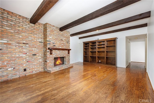 unfurnished living room with a brick fireplace, baseboards, beamed ceiling, and wood finished floors