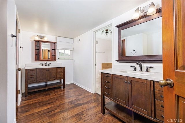 bathroom with wood finished floors, two vanities, a sink, and baseboards