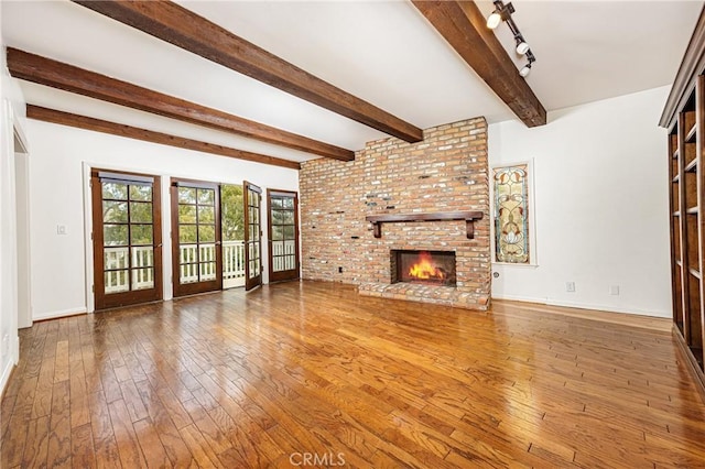unfurnished living room featuring a fireplace, wood-type flooring, baseboards, and beamed ceiling