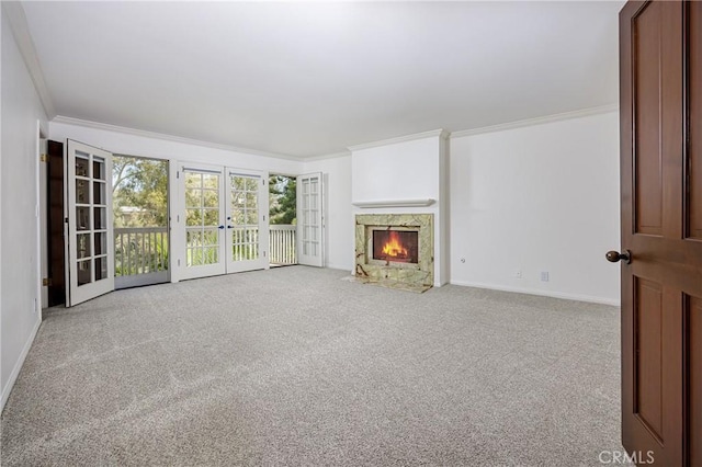 unfurnished living room with carpet, a fireplace with flush hearth, ornamental molding, french doors, and baseboards