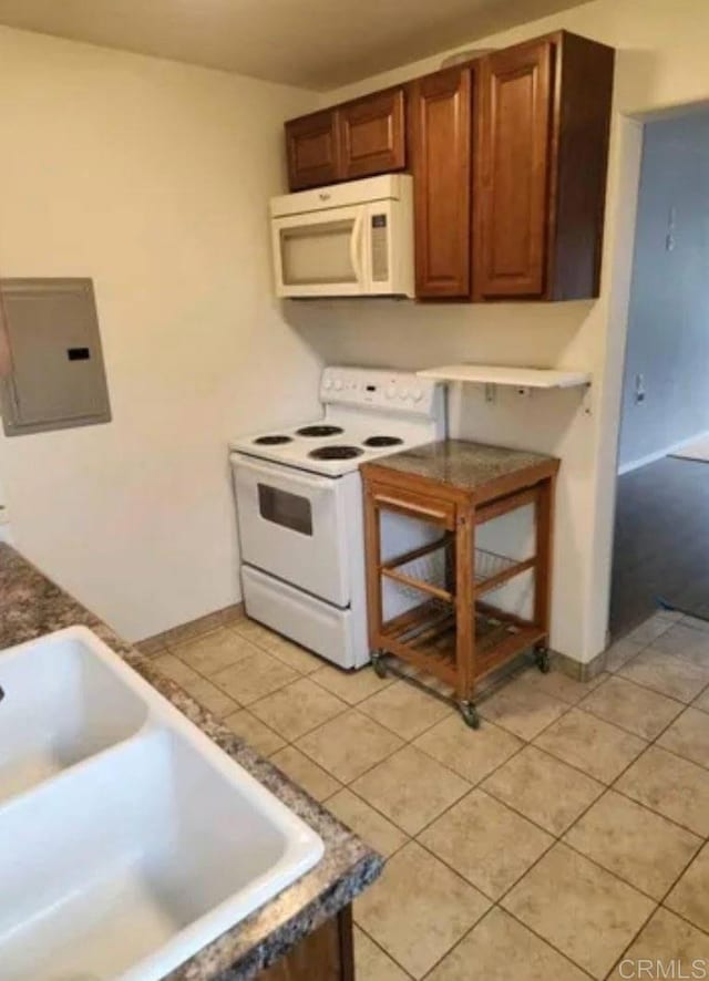 kitchen featuring electric panel, a sink, light tile patterned floors, baseboards, and white appliances