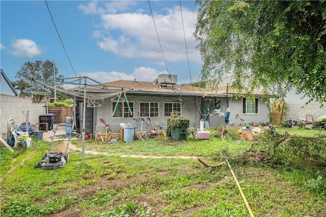 rear view of house featuring a yard, stucco siding, and fence