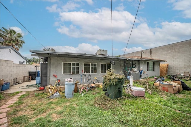 back of property with stucco siding, fence, and a lawn