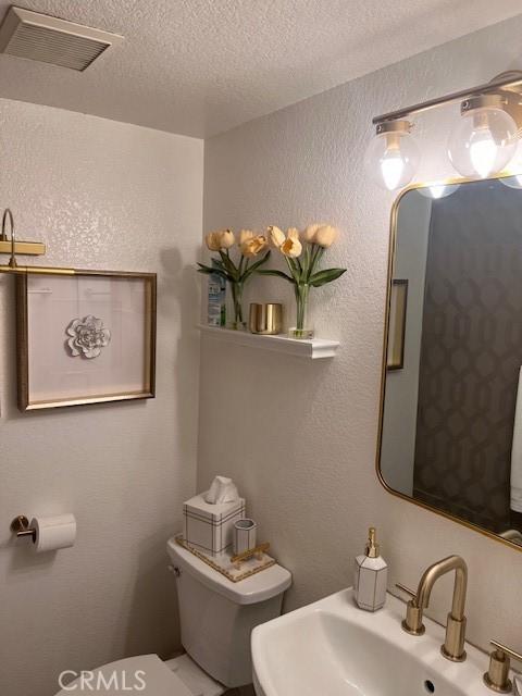 2899 Amber Dr, Corona, CA 92882 - half bathroom featuring a textured wall, visible vents, toilet, a sink, and a textured ceiling