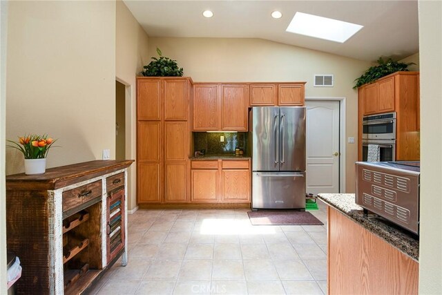 24182 Via Llano, Murrieta, CA 92562 - kitchen featuring stainless steel appliances, a skylight, vaulted ceiling, dark stone counters, and tasteful backsplash