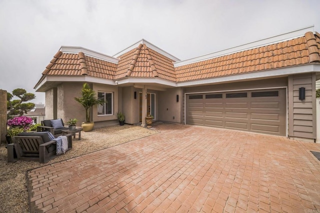 view of front of property featuring an attached garage, stucco siding, a tile roof, and decorative driveway