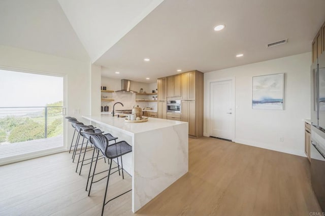 kitchen featuring visible vents, oven, open shelves, wall chimney range hood, and a breakfast bar area