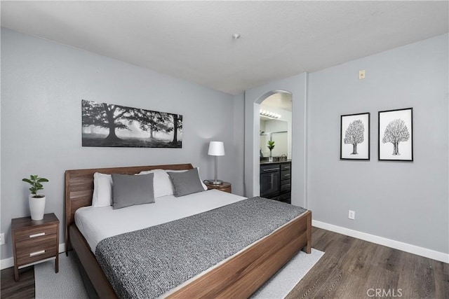 bedroom with arched walkways, dark wood finished floors, baseboards, and connected bathroom
