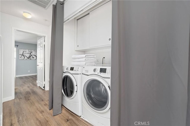 laundry area with light wood-style flooring, washer and clothes dryer, baseboards, visible vents, and cabinet space