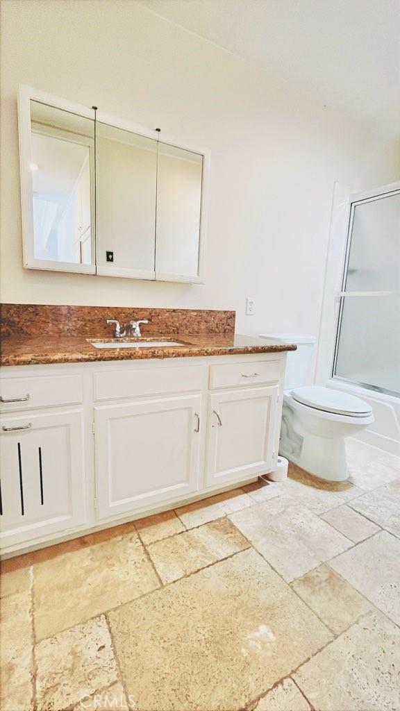 2019 Via Mariposa W Unit G, Laguna Woods, CA 92637 - full bathroom featuring stone tile floors, vanity, toilet, and combined bath / shower with glass door