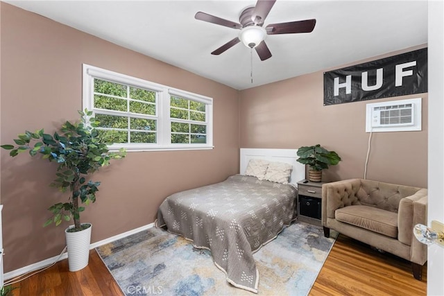 bedroom featuring wood finished floors, a wall mounted air conditioner, baseboards, and a ceiling fan