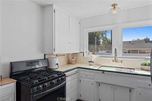kitchen featuring white cabinets, gas range, a sink, tile counters, and decorative backsplash