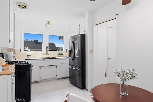 kitchen with white cabinets, gas stove, light countertops, a sink, and stainless steel fridge