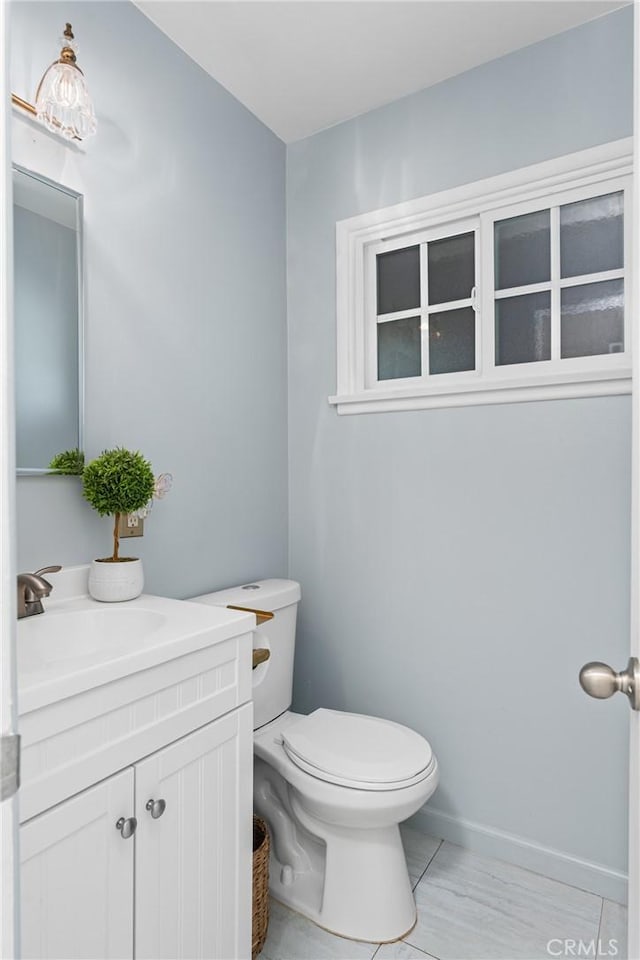 half bathroom with tile patterned floors, toilet, vanity, and baseboards