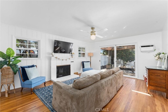 living room featuring a wall mounted air conditioner, a fireplace, a ceiling fan, and wood finished floors