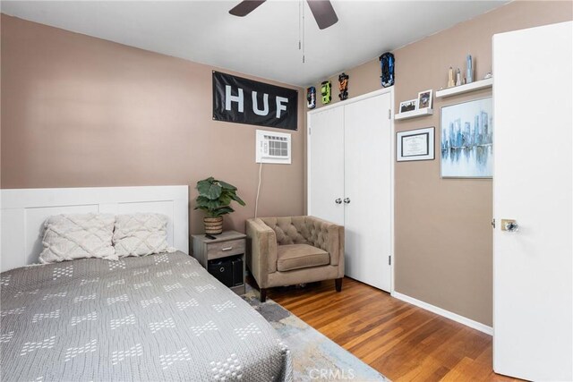 bedroom featuring a closet, baseboards, an AC wall unit, a ceiling fan, and wood finished floors