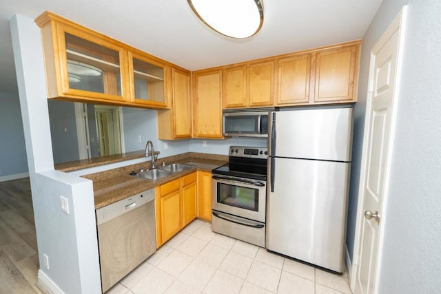 kitchen with appliances with stainless steel finishes, a sink, glass insert cabinets, and dark stone counters