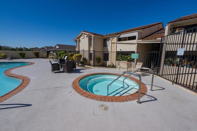 community pool with fence, a community hot tub, and a patio