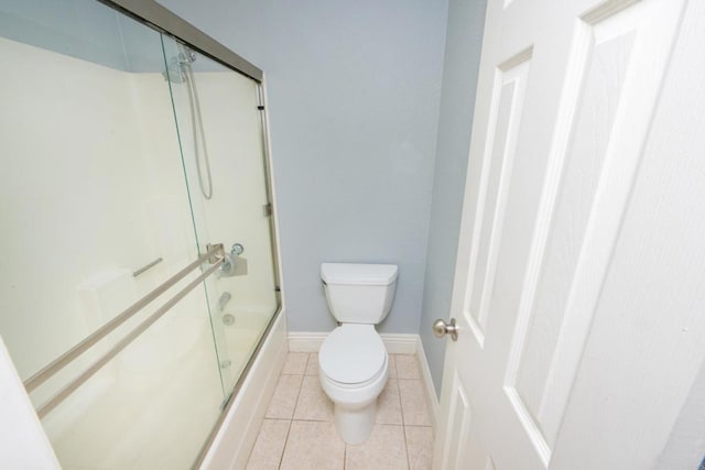 full bathroom featuring toilet, bath / shower combo with glass door, tile patterned flooring, and baseboards