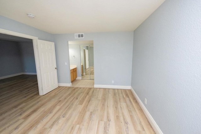unfurnished bedroom featuring light wood-type flooring, baseboards, and connected bathroom