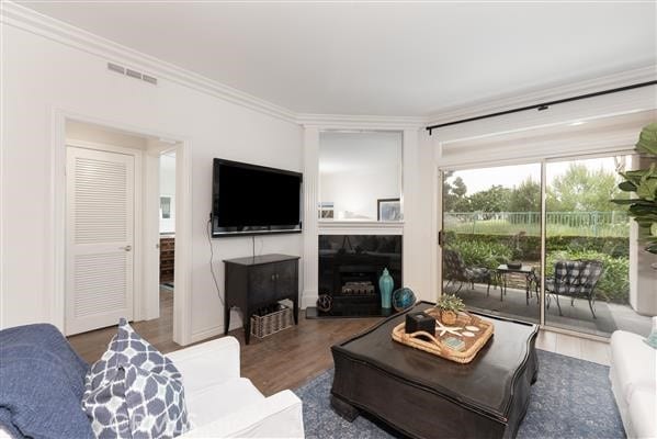 living room featuring a tiled fireplace, visible vents, ornamental molding, and wood finished floors