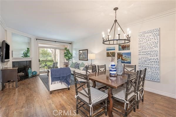 dining room featuring a notable chandelier, baseboards, a fireplace, crown molding, and wood finished floors