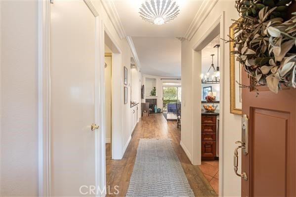 corridor featuring ornamental molding, a notable chandelier, and wood finished floors