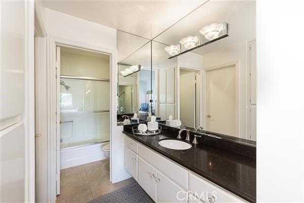 bathroom with toilet, tile patterned floors, shower / bath combination with glass door, and vanity