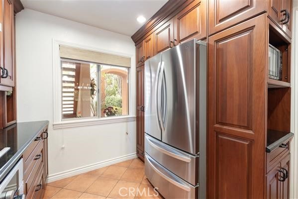 kitchen with baseboards, recessed lighting, light tile patterned floors, freestanding refrigerator, and brown cabinets