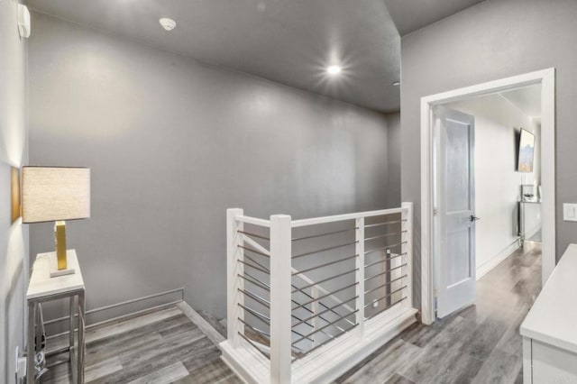 hall featuring baseboards, wood finished floors, recessed lighting, and an upstairs landing
