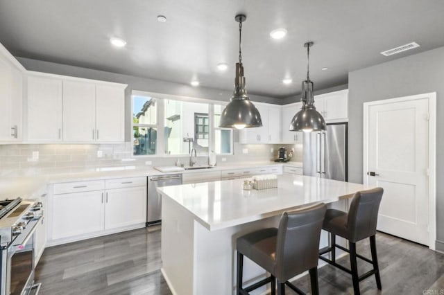 kitchen with dark wood finished floors, visible vents, a sink, high quality appliances, and decorative backsplash
