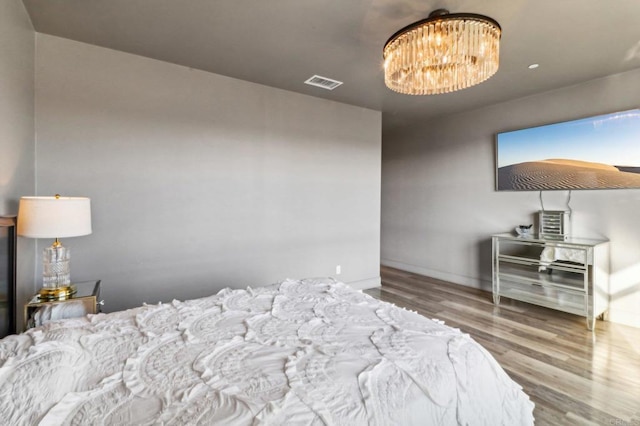 bedroom with baseboards, a notable chandelier, wood finished floors, and visible vents