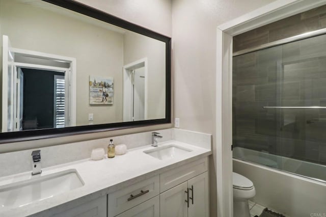 bathroom with combined bath / shower with glass door, a sink, double vanity, and toilet