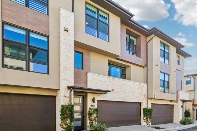 multi unit property with stucco siding, an attached garage, and stone siding