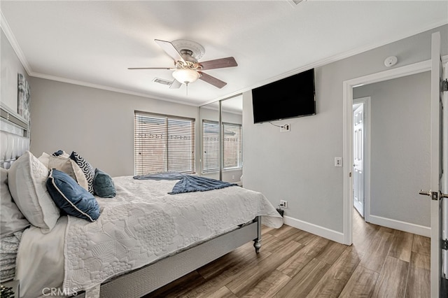bedroom with a ceiling fan, ornamental molding, visible vents, wood finished floors, and baseboards