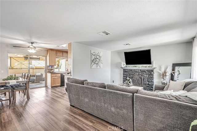 living area with visible vents, ceiling fan, a textured ceiling, a fireplace, and wood finished floors