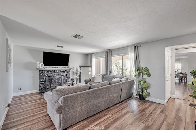 living room featuring a fireplace, a textured ceiling, visible vents, light wood finished floors, and baseboards