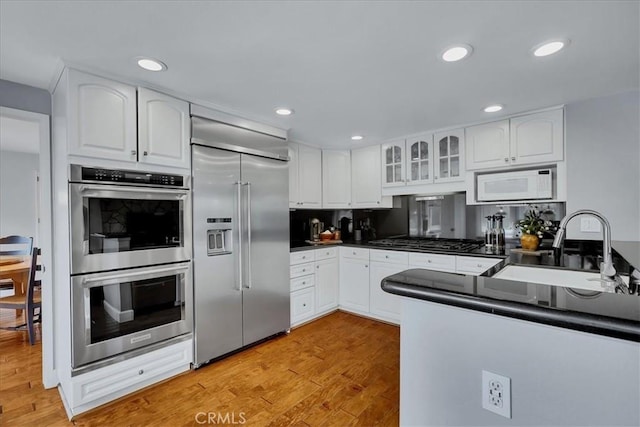 kitchen with glass insert cabinets, white cabinetry, dark countertops, stainless steel appliances, and a sink