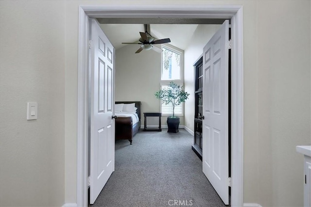 corridor featuring dark colored carpet, baseboards, and vaulted ceiling