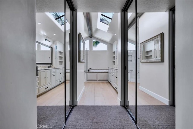 full bath featuring baseboards, wood finished floors, vanity, and lofted ceiling with skylight