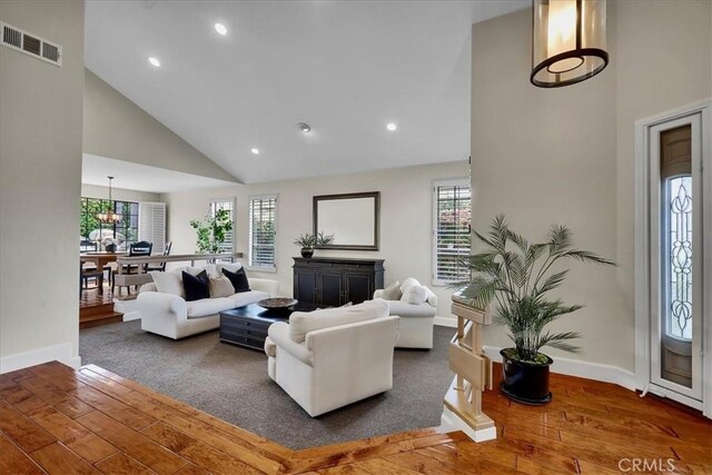 living area featuring visible vents, high vaulted ceiling, hardwood / wood-style flooring, and a healthy amount of sunlight