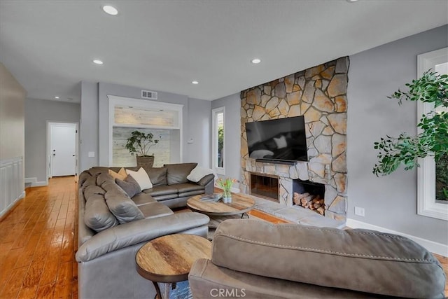 living area with a stone fireplace, baseboards, recessed lighting, visible vents, and light wood finished floors