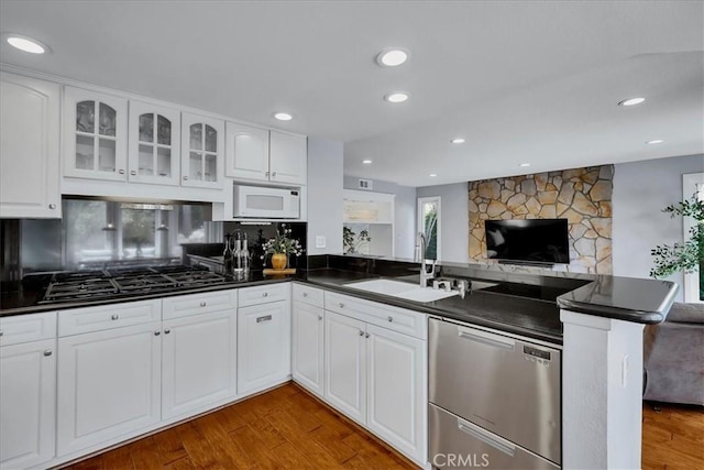 kitchen with white microwave, dishwasher, dark countertops, and a peninsula