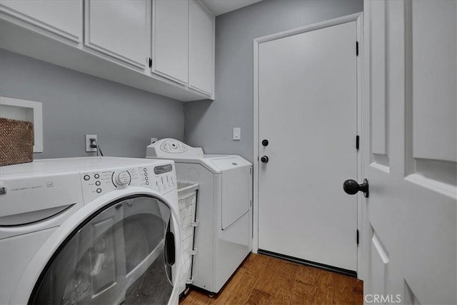clothes washing area with washing machine and dryer, wood finished floors, and cabinet space