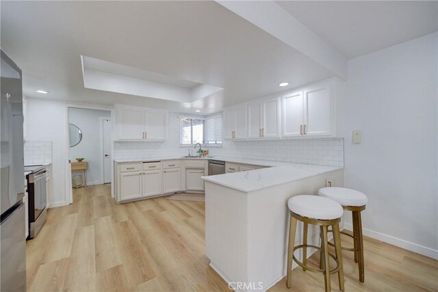 4210 Sirius Ave, Lompoc, CA 93436 - kitchen with white cabinets, light wood-type flooring, appliances with stainless steel finishes, a breakfast bar, and a peninsula